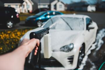 an arm holding onto a hose aimed towards a sudsy car