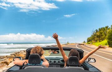 Two people riding in a convertible with the top down on a sunny summer day